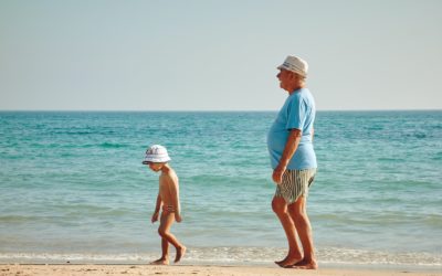 man in blue shirt standing on seashore near boy in white hat